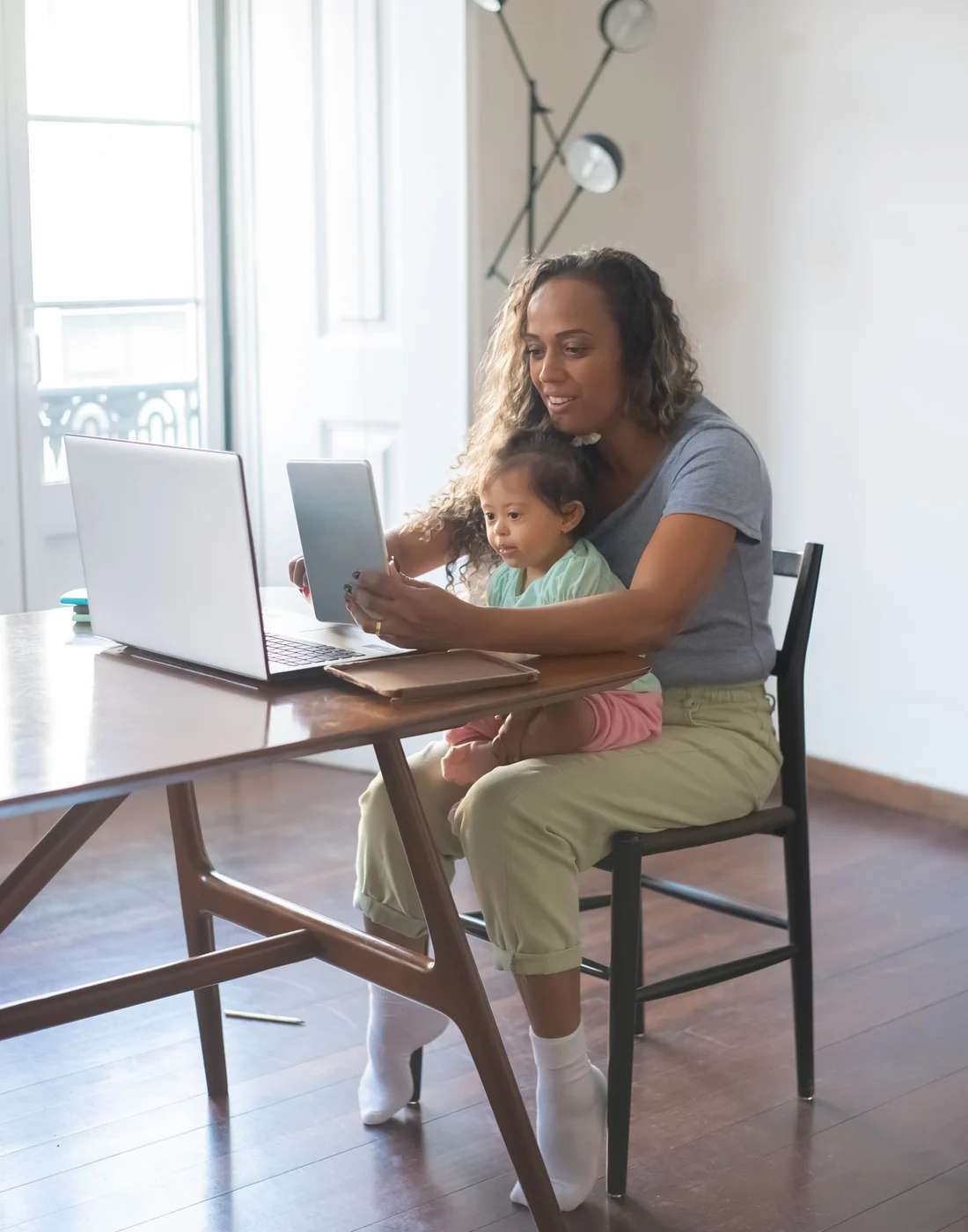 A parent working at a laptop with her toddler on her lap