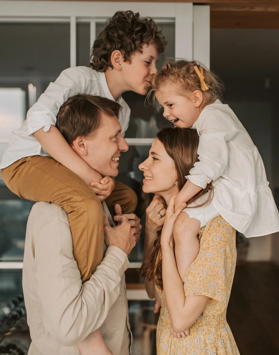 Two parents at home with their son and daughter on their shoulders