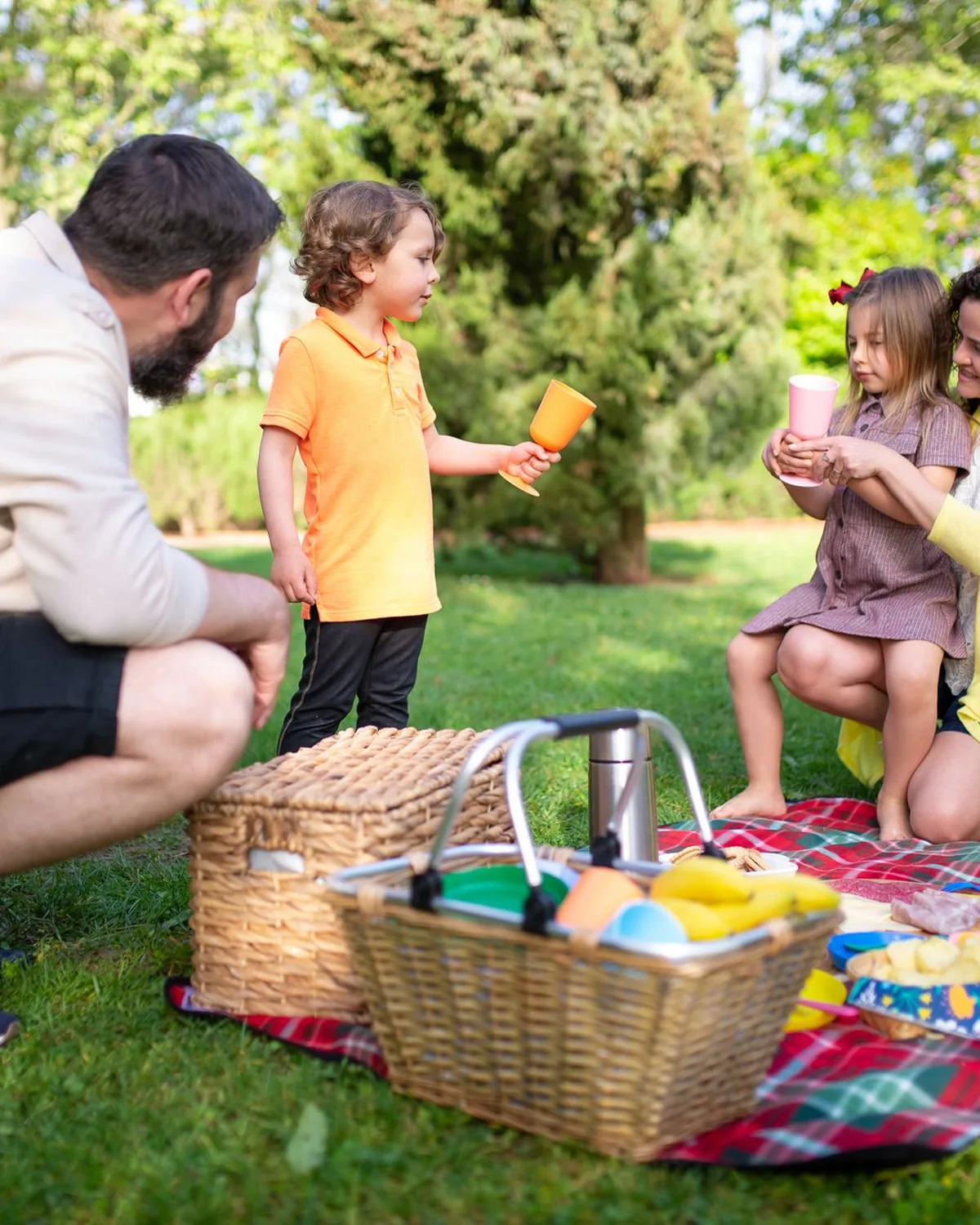 Two parents and their two children sharing a picnic on the grass in a park