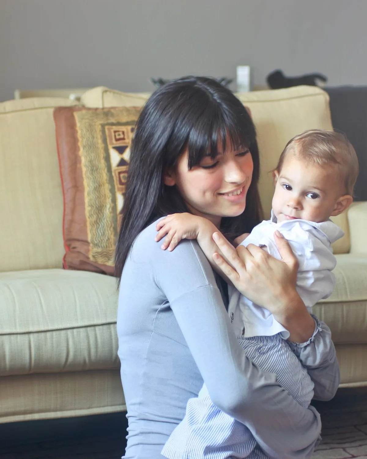 A babysitter smiling with a baby in her arms in a family living room