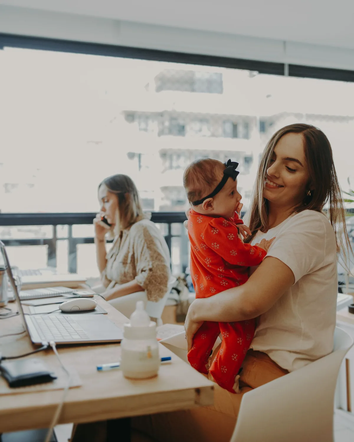A parent holding her small child while working alongside a colleague