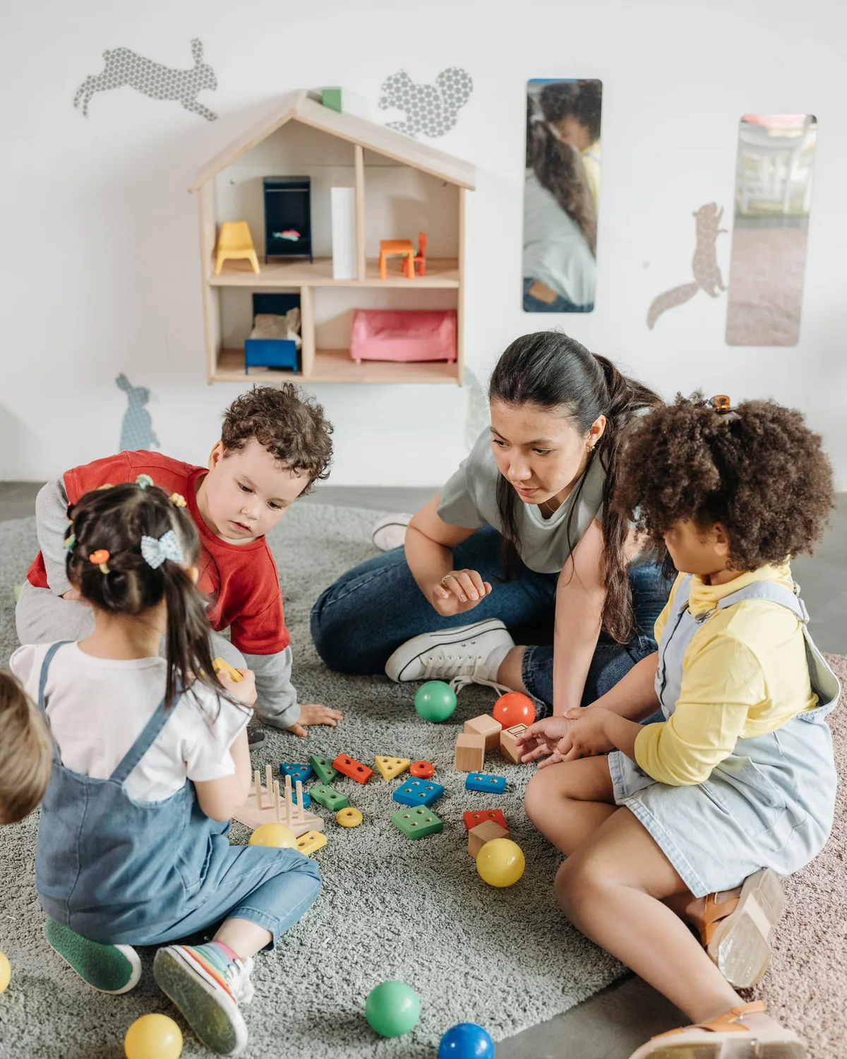 An early years worker sitting on the floor playing with three young children and their toys
