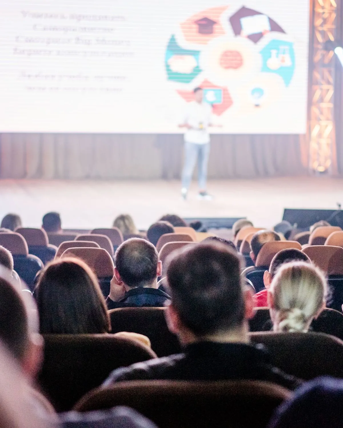 An audience seated in a conference hall facing a lit stage