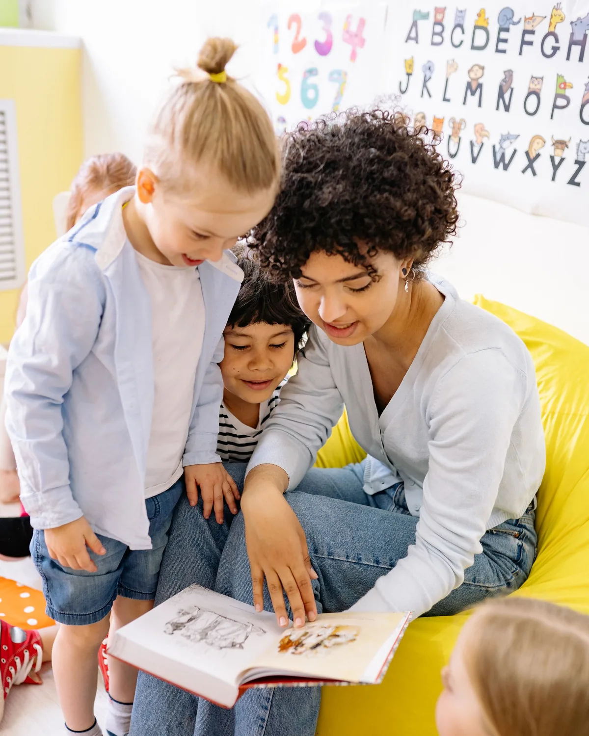A caregiver sitting on the floor looking at a book with two children
