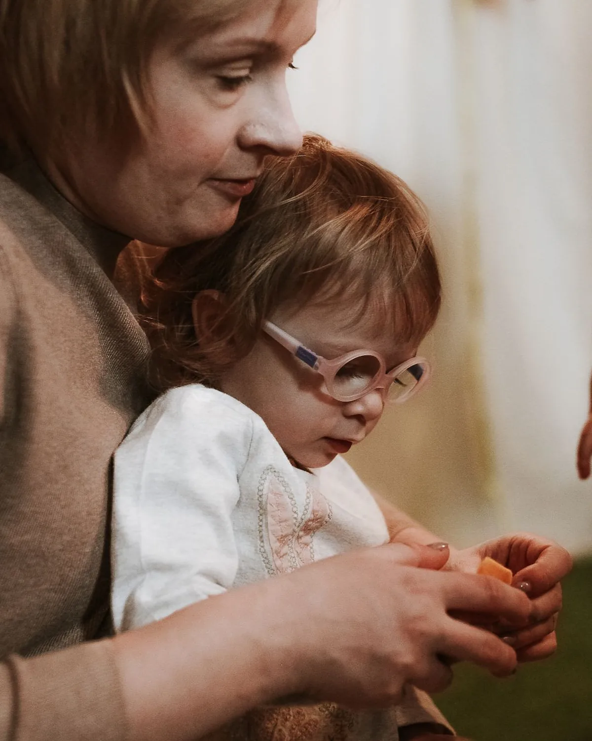 A caregiver holding a young child wearing glasses, close and calm
