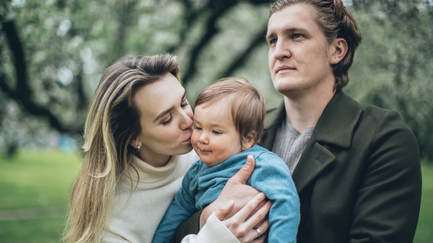 A mother kissing her baby while her partner looks on