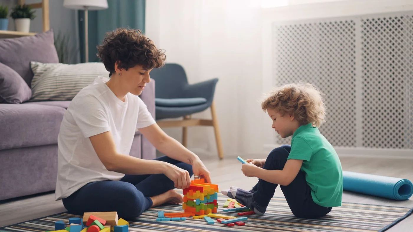 A caregiver and a young boy building with coloured blocks