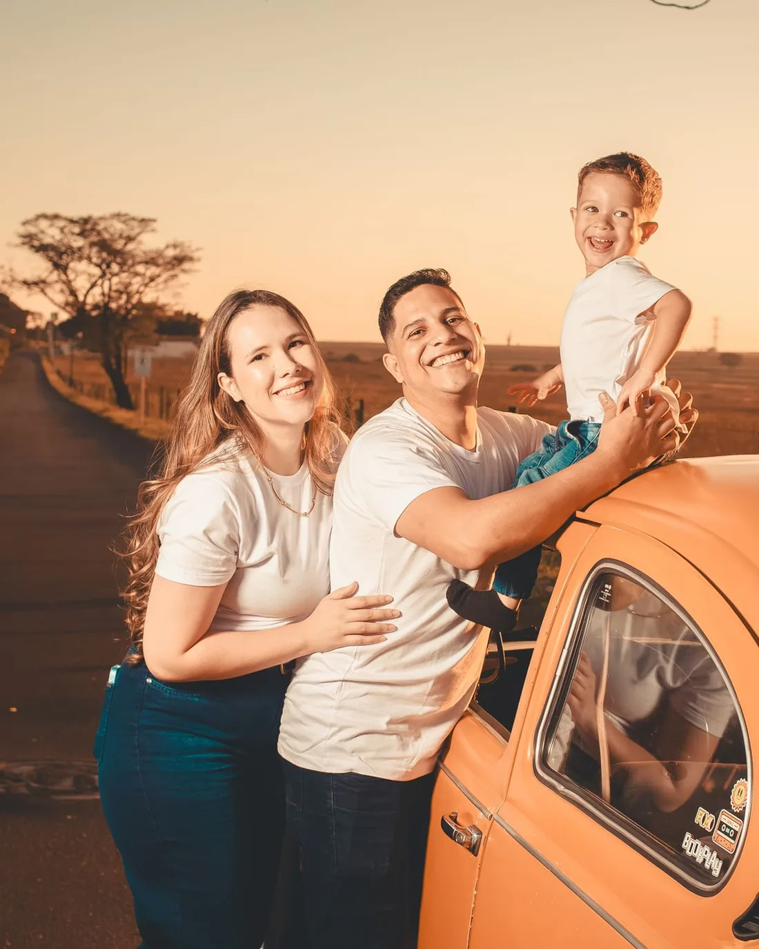 A family with their young child beside their car at sunset