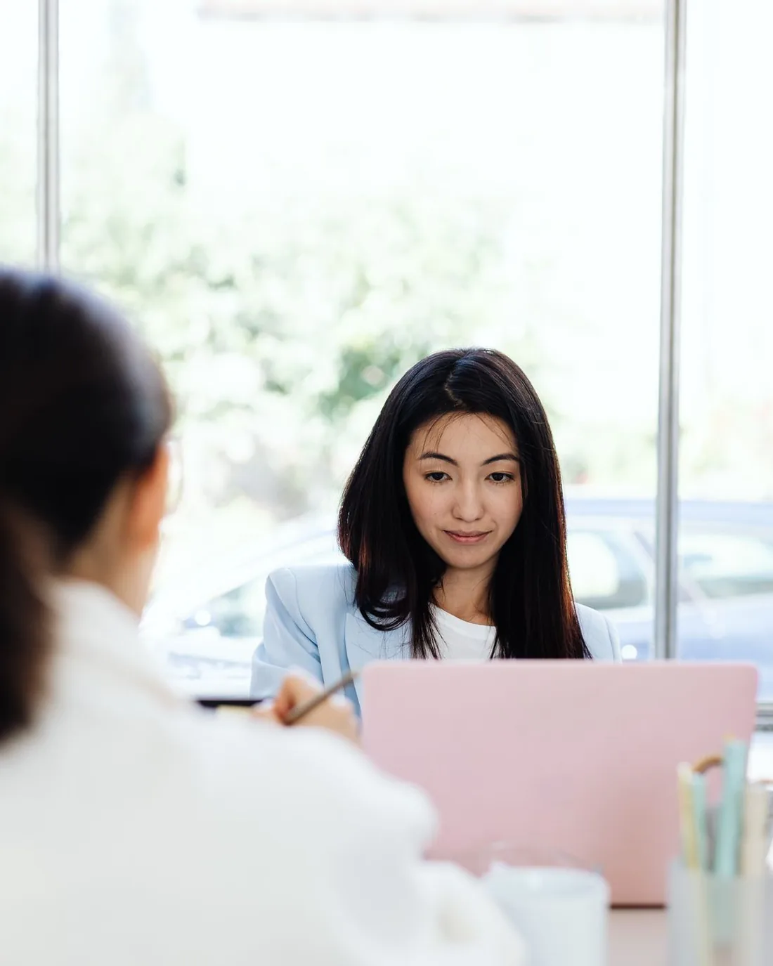 Two women in conversation across a table with laptops open