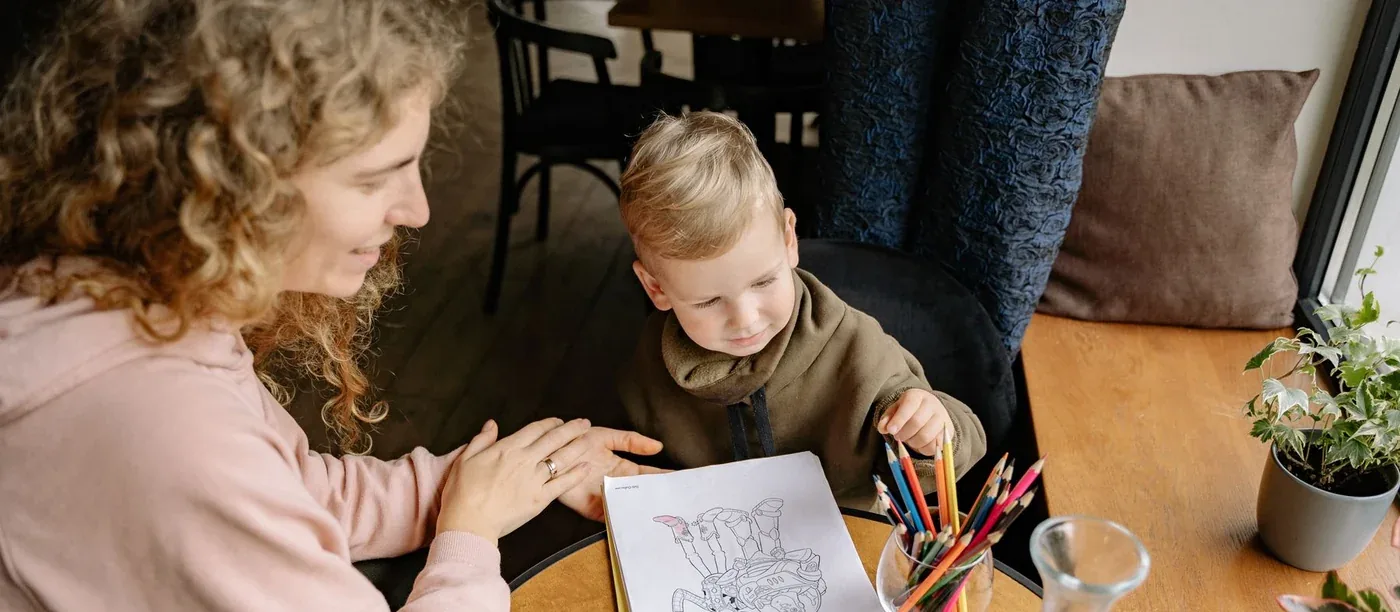 A caregiver colouring at a table with a young boy