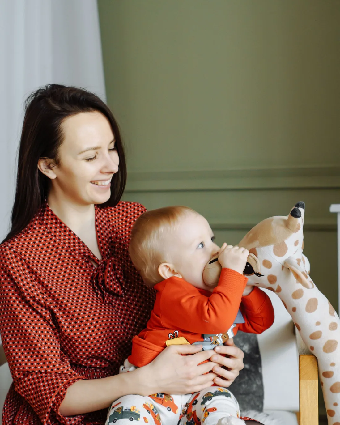 A caregiver smiling at a baby who is chewing on a soft toy