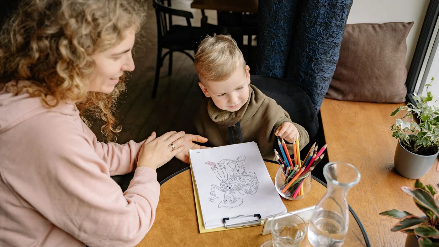 A caregiver colouring at a table with a young boy